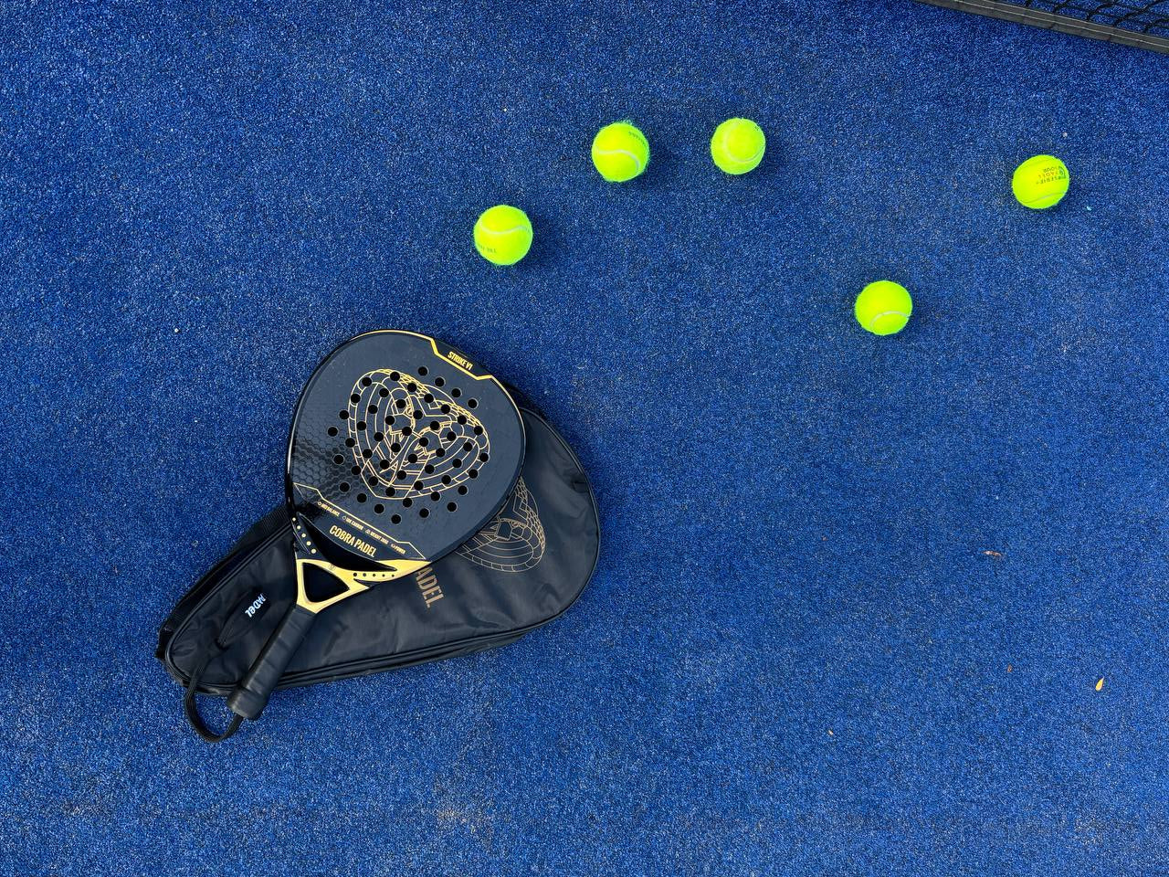 strike v1 cobra padel laying on blue padel court with balls